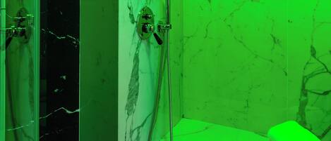 A bathroom with a glass shower enclosure, marble walls, and a green-lit vanity area.
