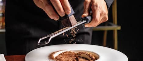 A person grating a substance into a bowl on a wooden table.