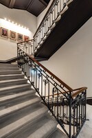 Una scala con ringhiera in metallo nero e corrimano in legno, che conduce a un piano superiore.