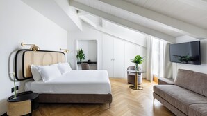 A modern bedroom with a bed, a sofa, a TV, and a small table with a plant.