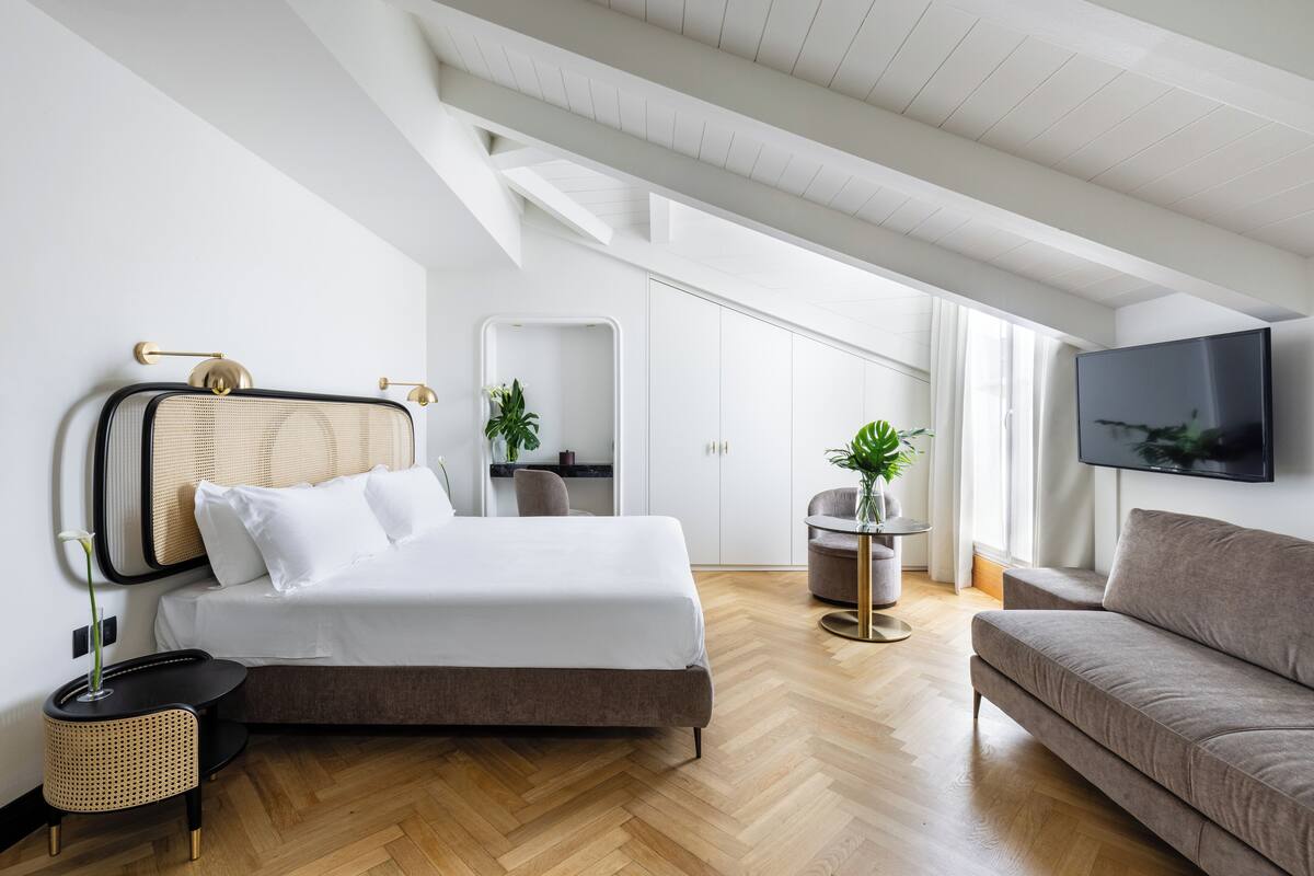 Un dormitorio moderno con cama, sofá, televisión y una mesita con una planta.