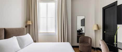A hotel room with a bed, a chair, a desk, and a large window with curtains.