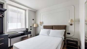 Une chambre d’hôtel moderne avec un grand lit, un bureau et une chaise. On y trouve deux tables de chevet avec des lampes, une fenêtre avec des rideaux et une armoire.