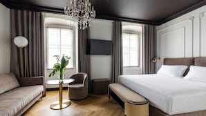 A modern hotel room with a large bed, a sofa, a round table with a plant, and a chandelier.