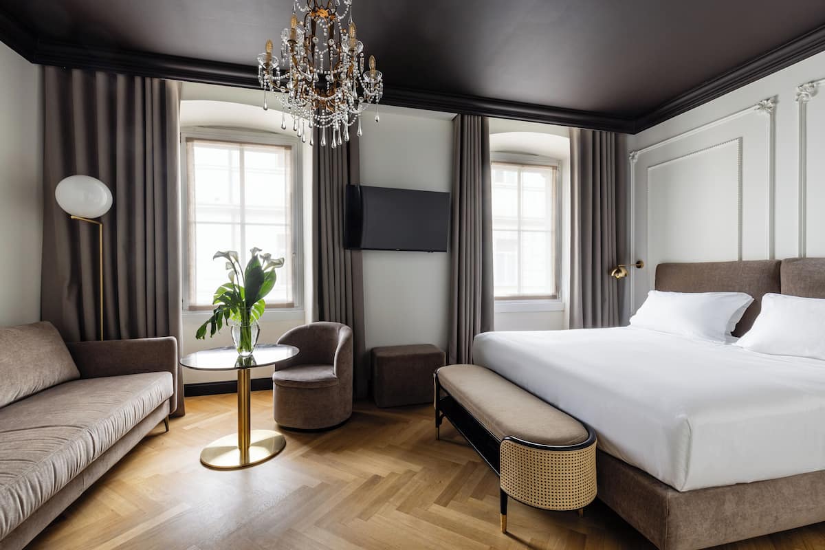 Una habitación de hotel moderna con una cama grande, un sofá, una mesa redonda con una planta y una araña.