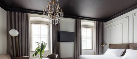 A modern hotel room with a large bed, a sofa, a round table with a plant, and a chandelier.
