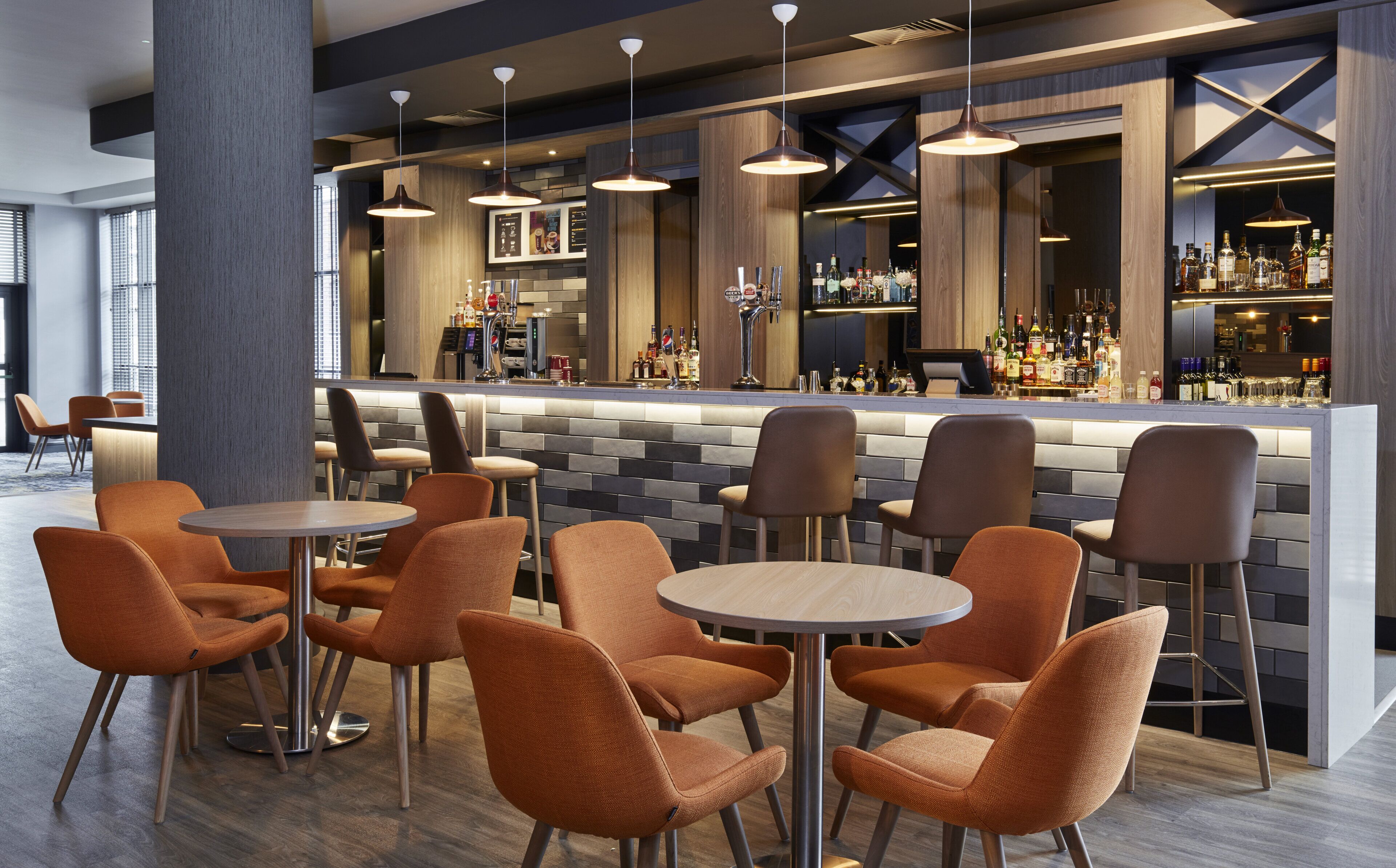 A bar area with multiple seating options, a bar counter with a variety of bottles, and pendant lighting.