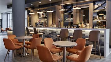 Zona de bar con diversas opciones de asientos, barra con una variedad de botellas e iluminación colgante.