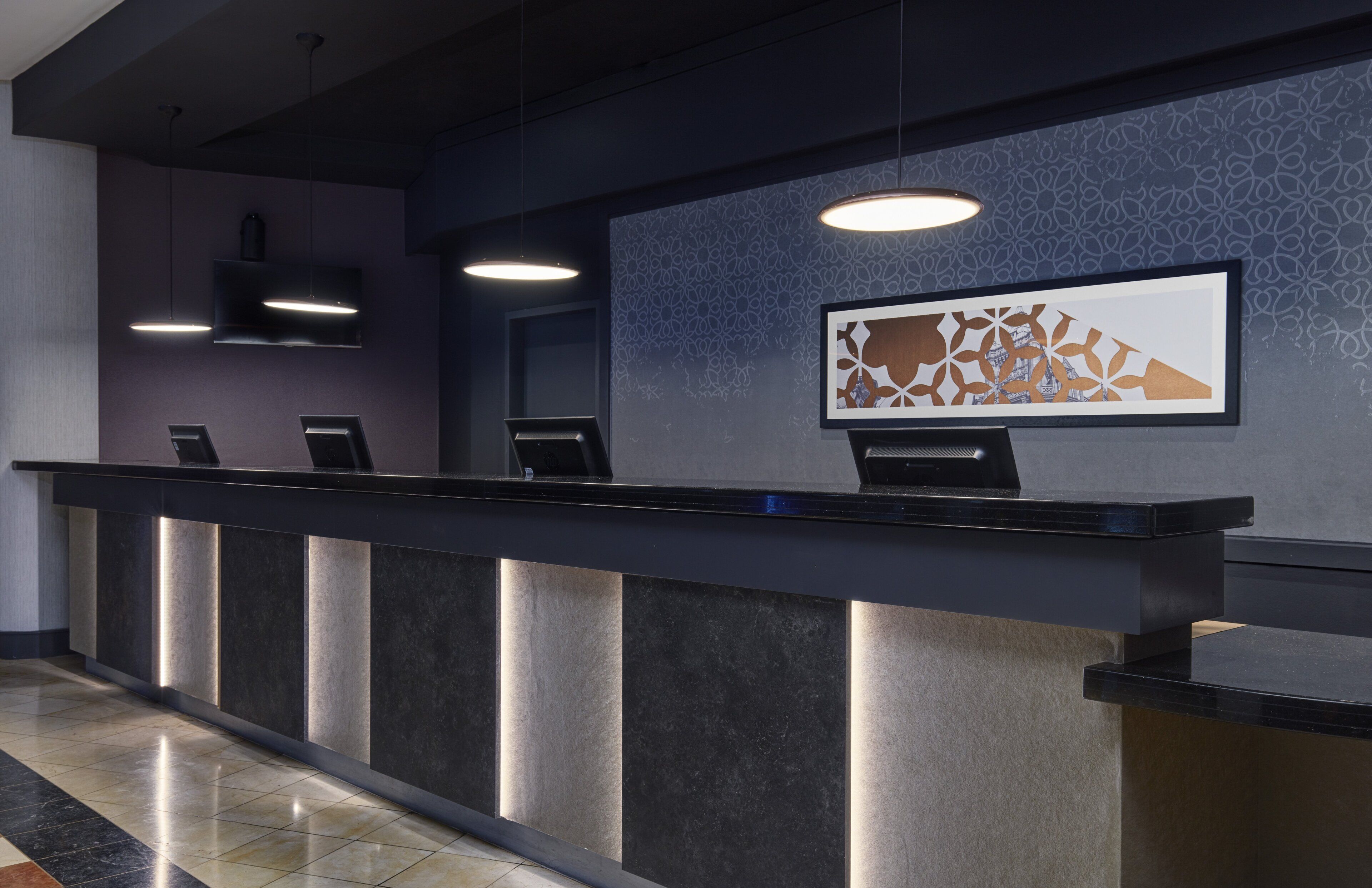Un comptoir d’accueil au design moderne, agrémenté d’un mur à motifs et d’une œuvre d’art encadrée placée au-dessus.