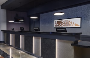 A reception desk with a modern design, featuring a patterned wall and a framed artwork above it.