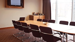 A conference room with a long table, eight chairs, a television on the wall, and a window with curtains.