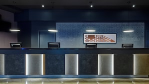 A reception desk with a modern design, featuring a dark blue wall with a geometric pattern, a flat-screen TV, and three pendant lights.