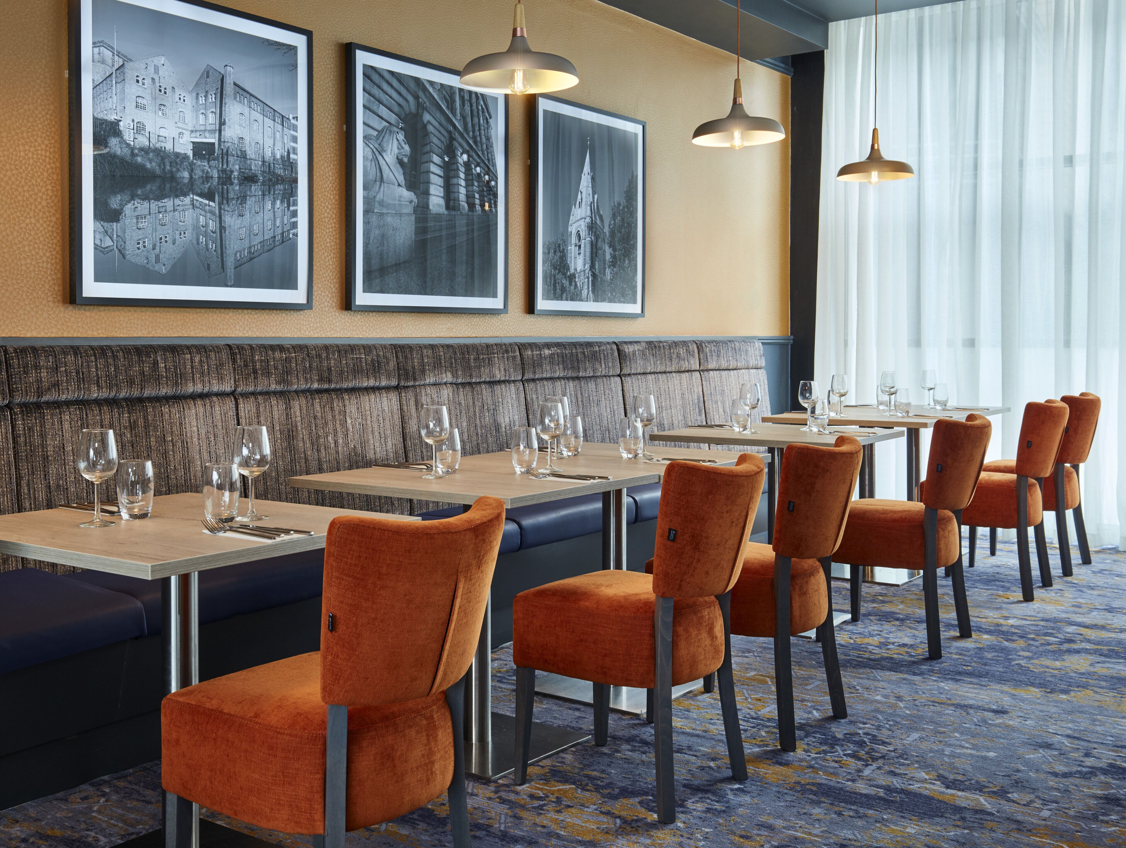 En restaurang med en lång bardisk, flera bord och orange klädda stolar.