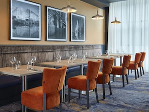 A restaurant with a long counter, multiple tables, and orange upholstered chairs.