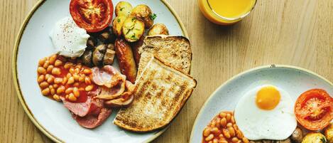 A breakfast plate with eggs, bacon, beans, mushrooms, tomatoes, and toast.