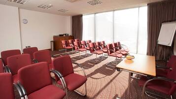 A conference room with red chairs, a wooden table, a whiteboard, and a clock on the wall.