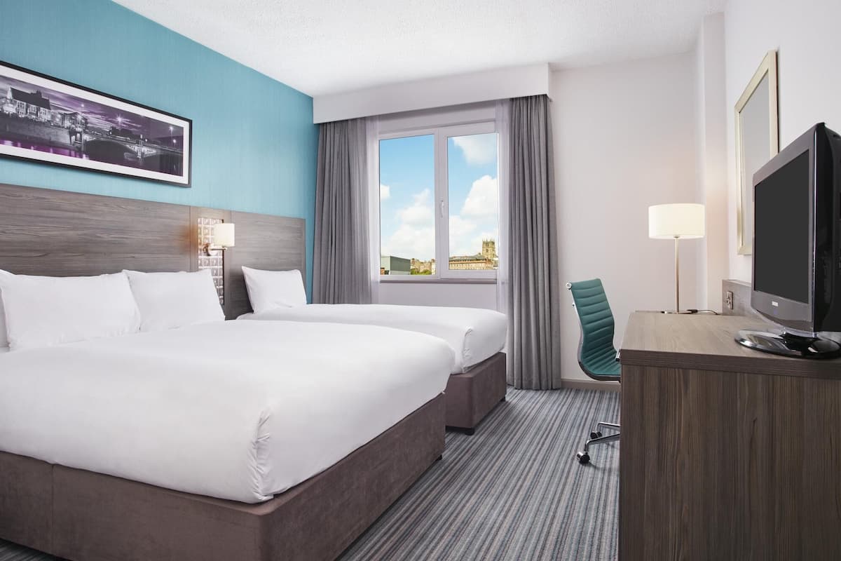 Ein Hotelzimmer mit Bett, Schreibtisch, Stuhl, Fernseher und einem Fenster mit Blick auf ein Gebäude.