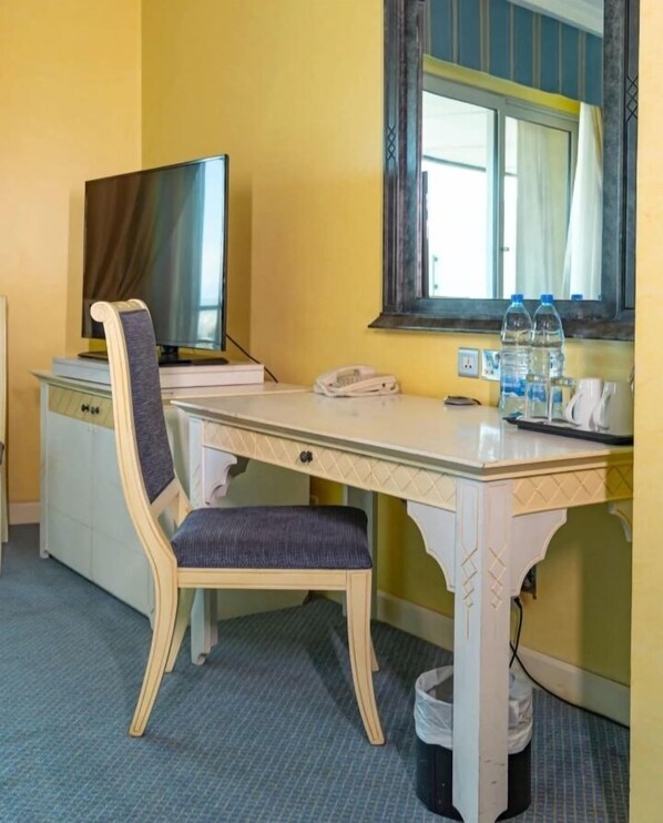 Una habitación de hotel con cama, escritorio y silla, televisión, ventana con cortinas y un cubo de basura.