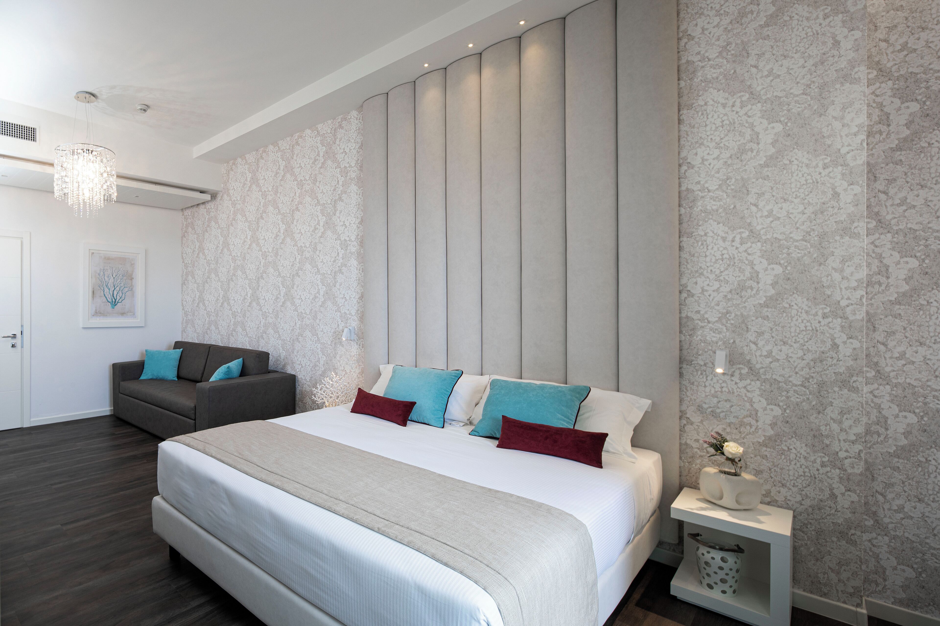 A modern bedroom with a large bed, a sofa, and a nightstand with a vase.