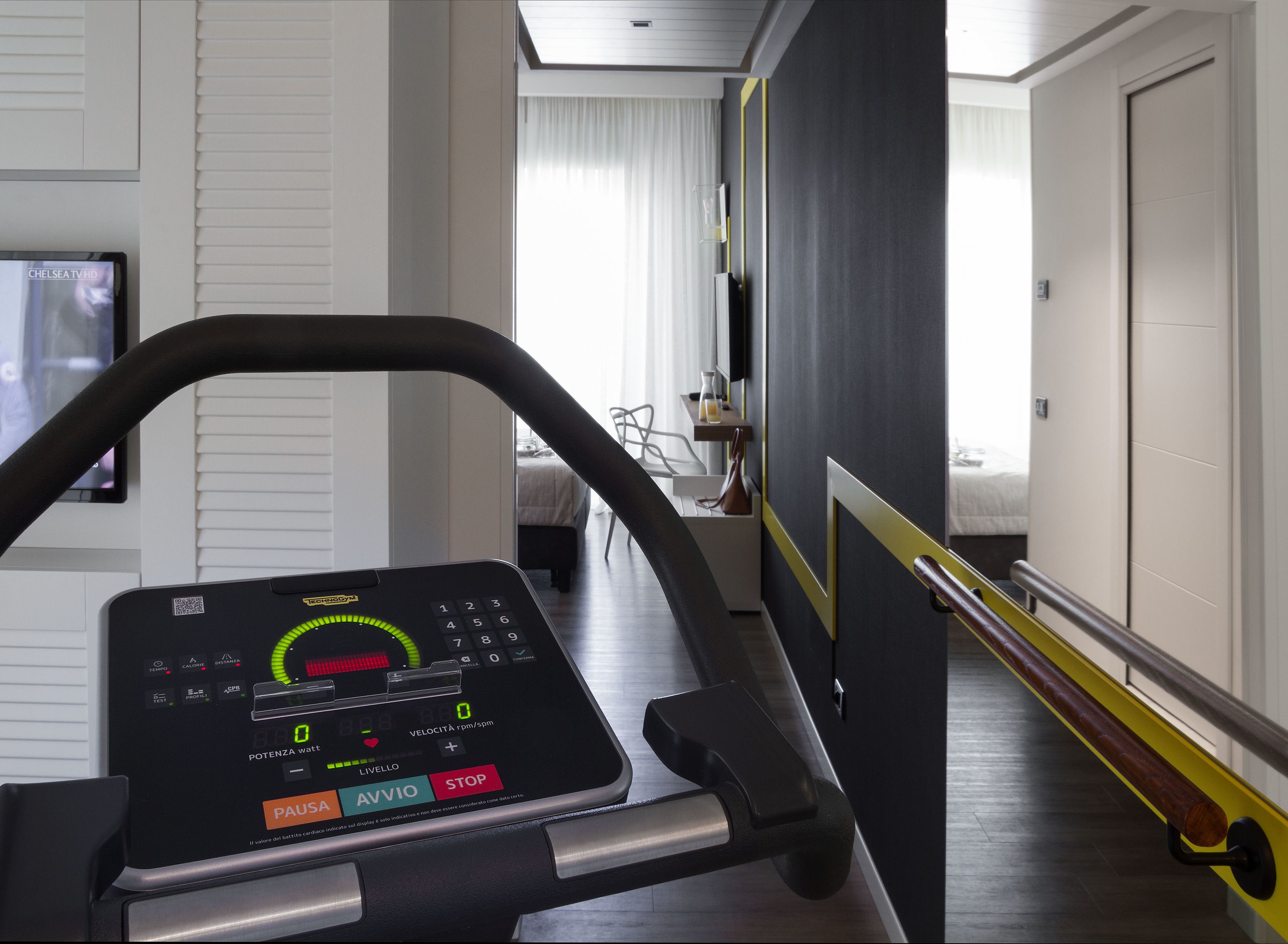 Una cinta de correr en una habitación de hotel, con una cama y un televisor al fondo.