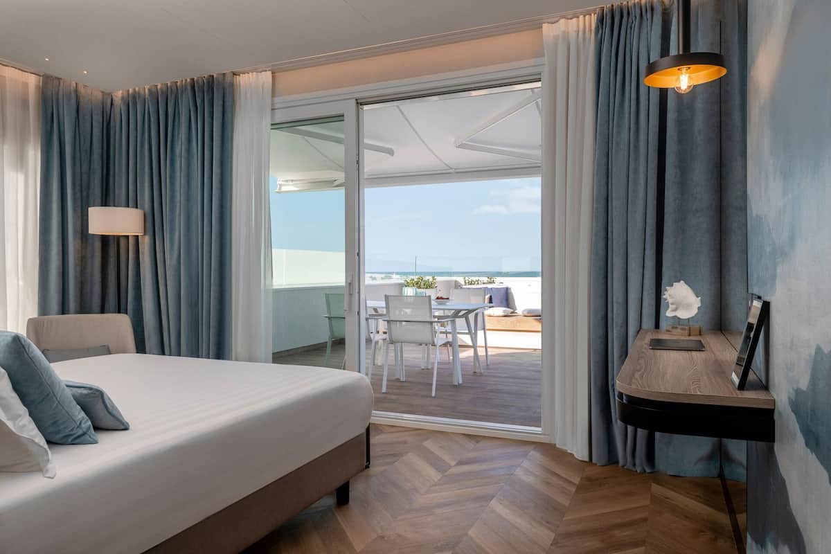 A bedroom with a bed, a desk, and a view of the balcony.
