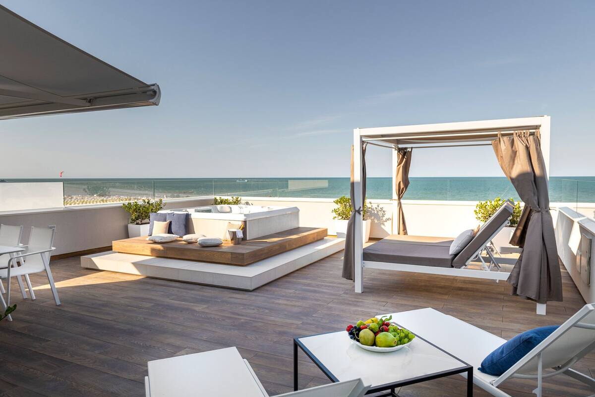 A rooftop terrace with a seating area, a table with fruit, and a view of the sea.