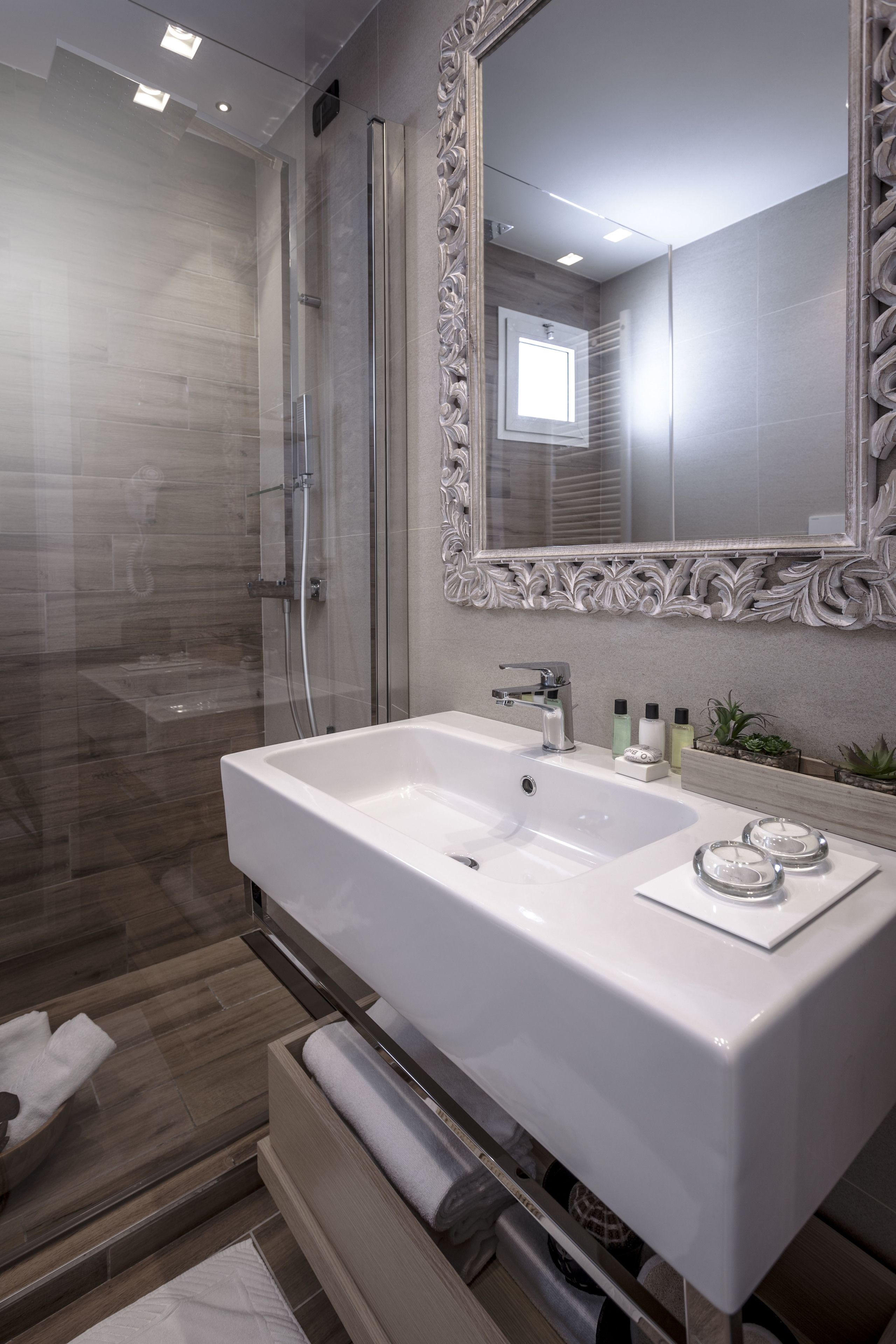 A modern bathroom with a large white sink, a glass shower enclosure, and a decorative mirror.