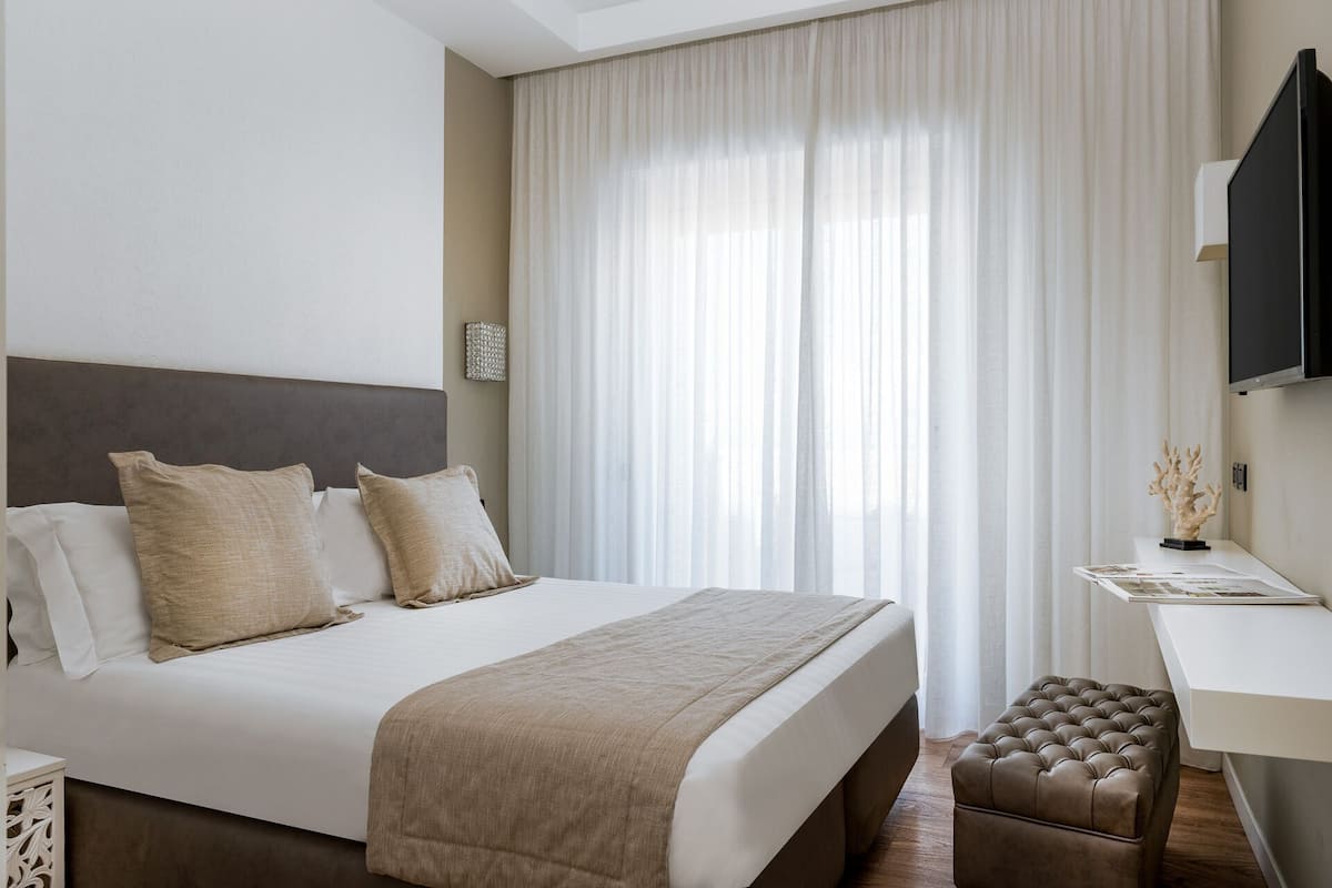 A hotel room with a large bed, a desk, a television, and a window with curtains.