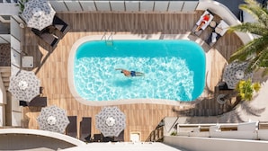 Piscina en la azotea con una persona nadando, rodeada de sillones de descanso y sombrillas.