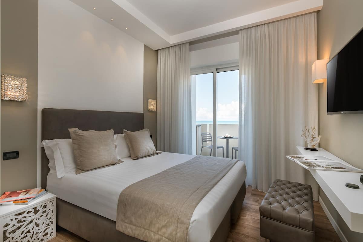 A modern hotel room with a large bed, a desk, a chair, and a TV.