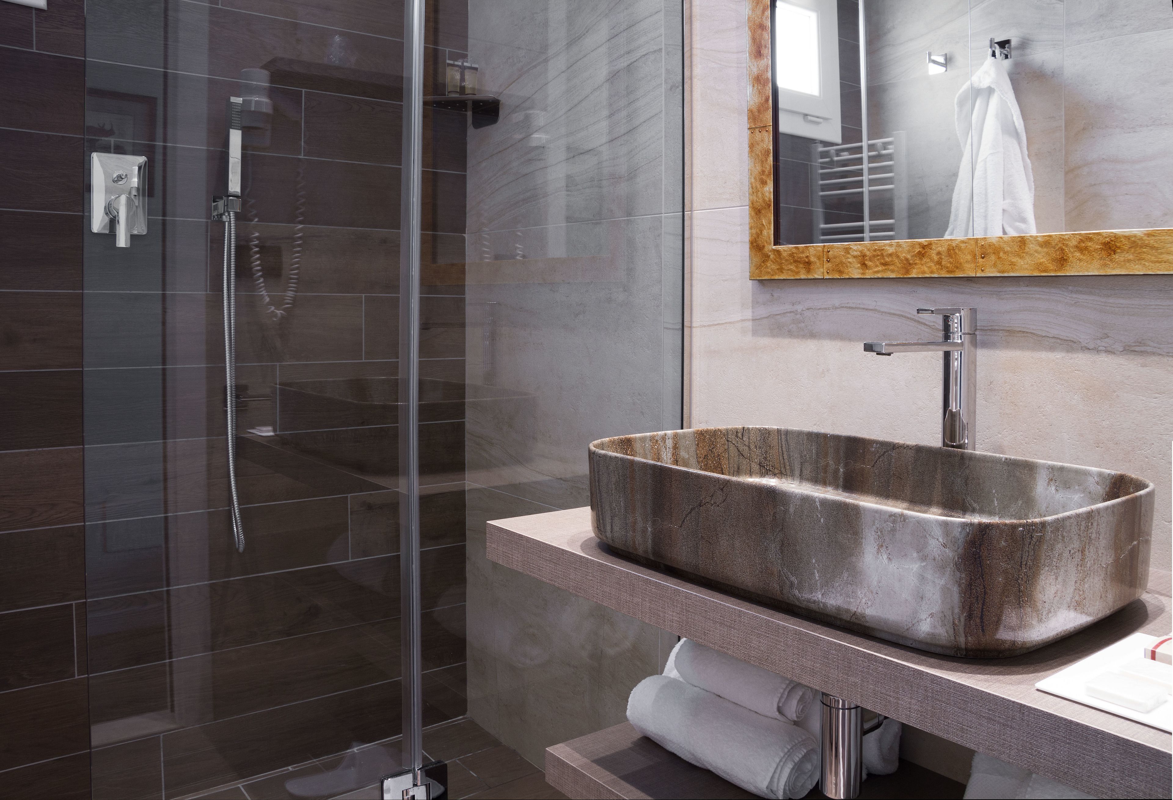 A modern bathroom with a glass-enclosed shower, a large rectangular stone sink, and a mirror with a wooden frame.