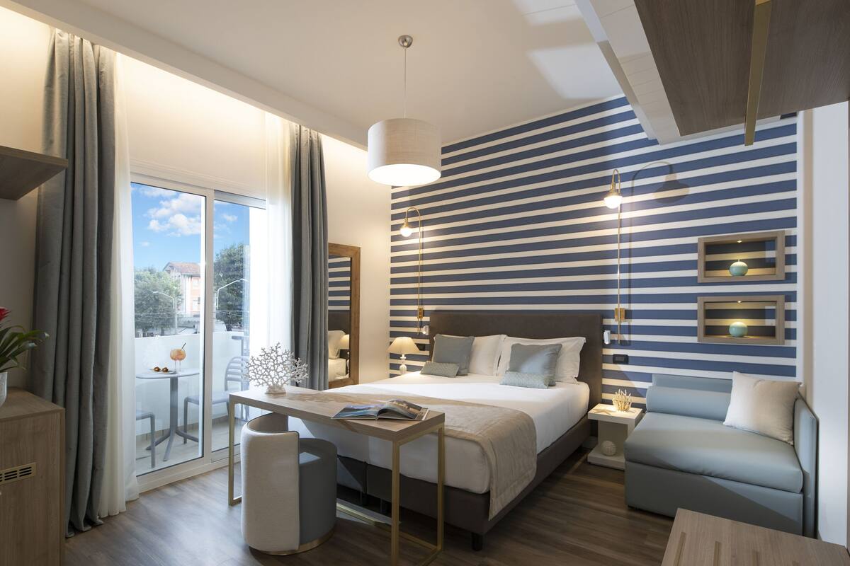 A modern bedroom with a large bed, bedside tables, a sofa, and a view of the outdoors.