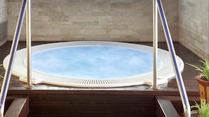 Een jacuzzi met metalen relingen, gelegen voor een stenen muur en houten vloer.