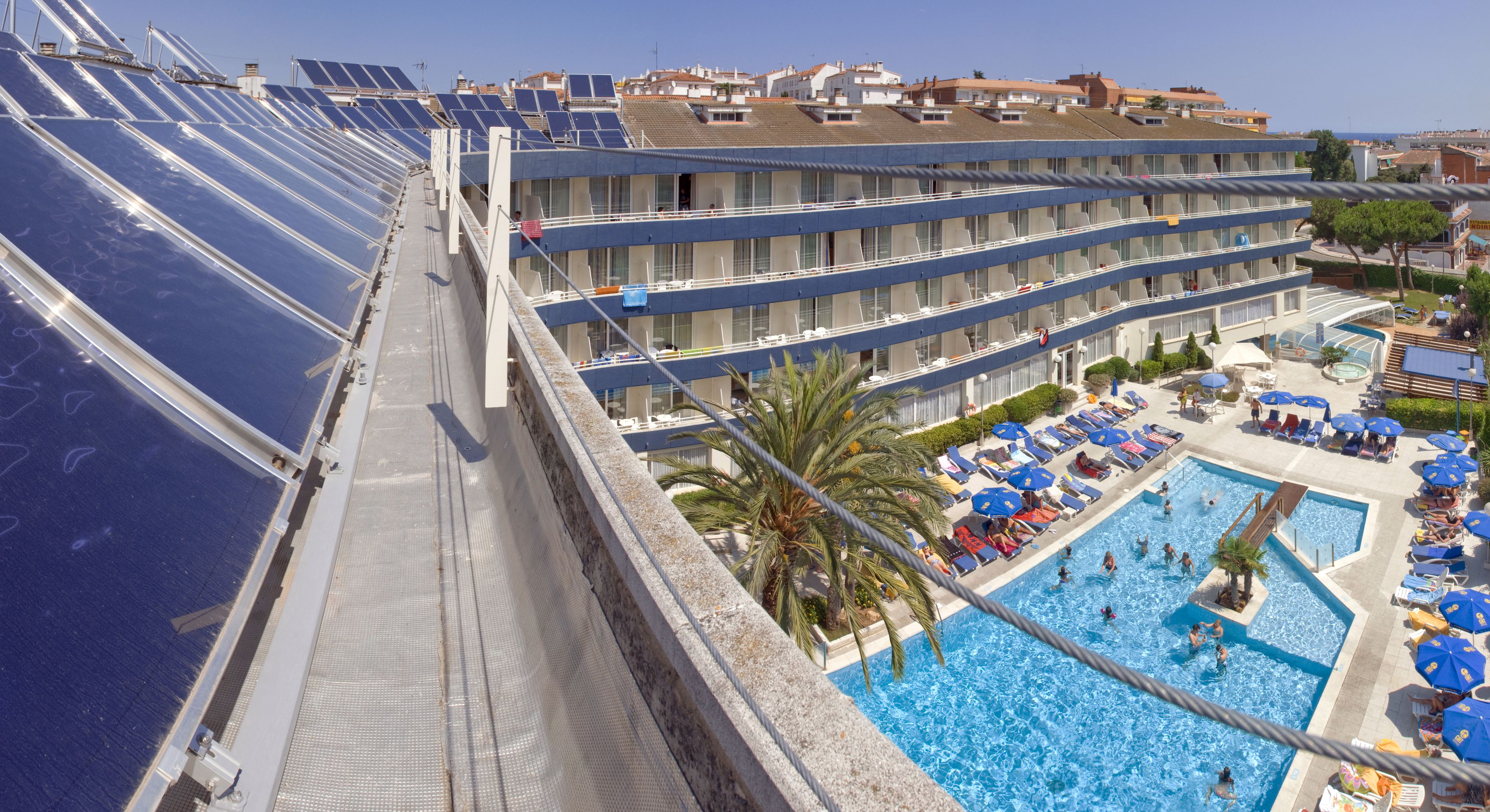 Um hotel com vários andares, uma piscina no terraço e painéis solares.