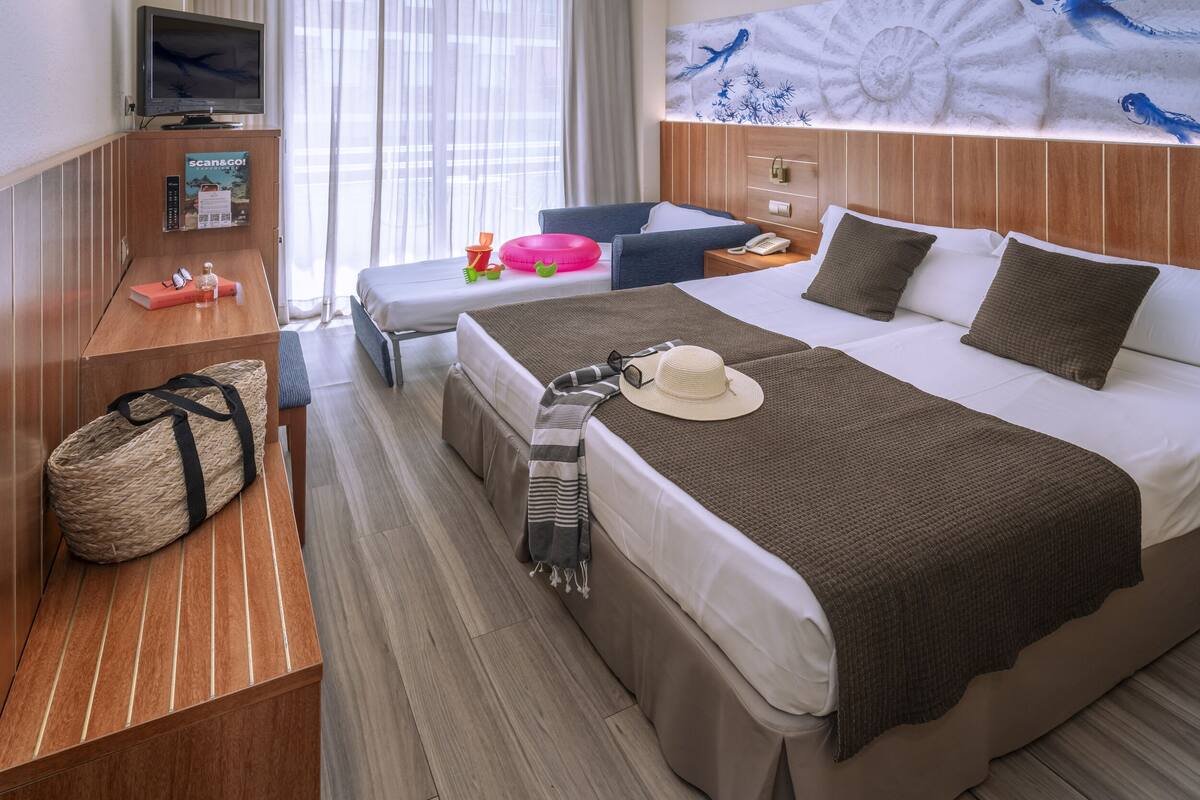 Hotelkamer met een bed, nachtkastje en een klein bureau met een televisie, afstandsbediening en een tijdschrift.