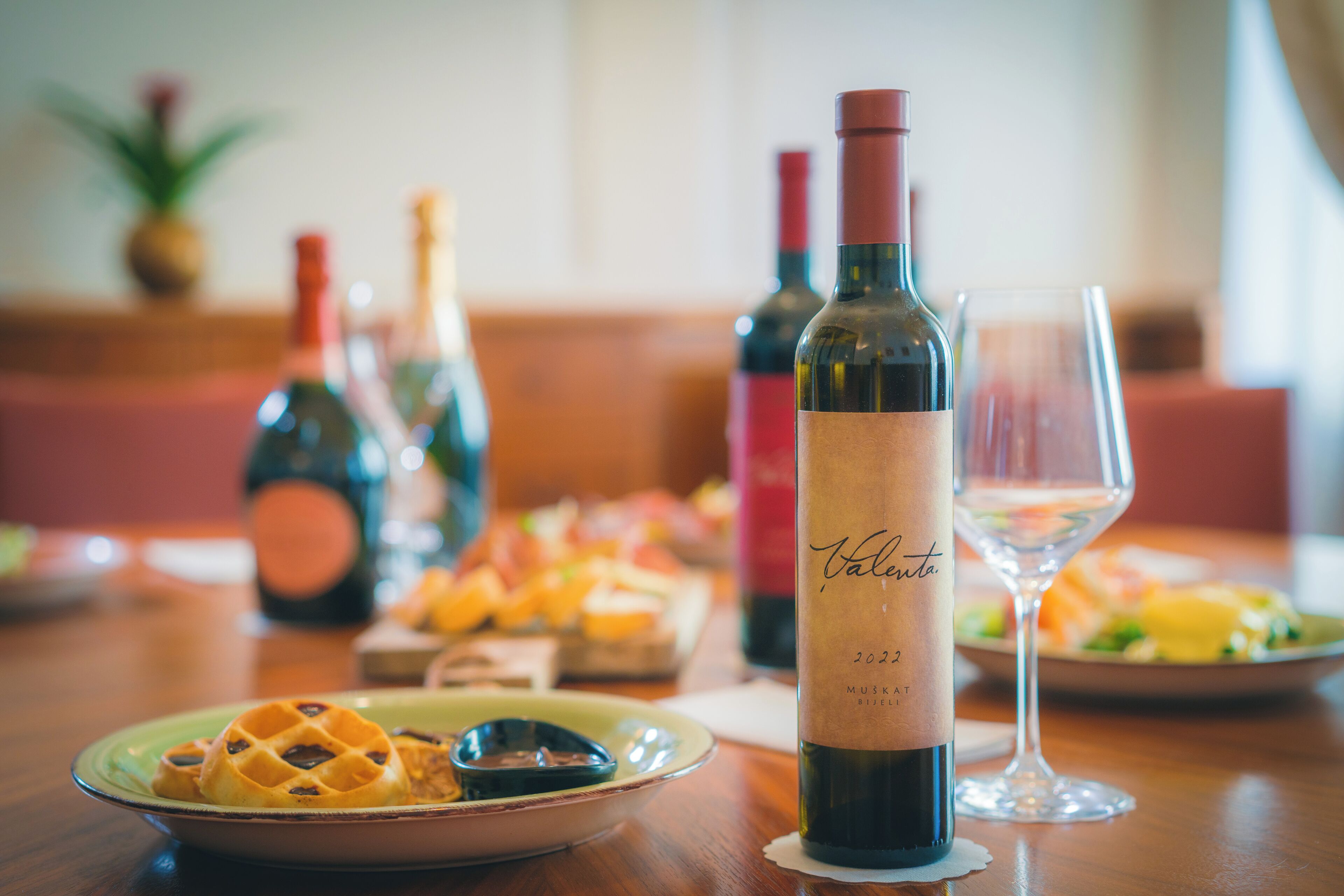 A dining table with a bottle of wine, a glass, and plates of food.