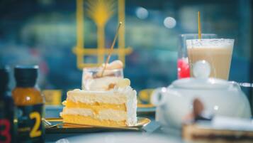 A dessert table with a slice of cake, a glass of iced coffee, and a teapot.