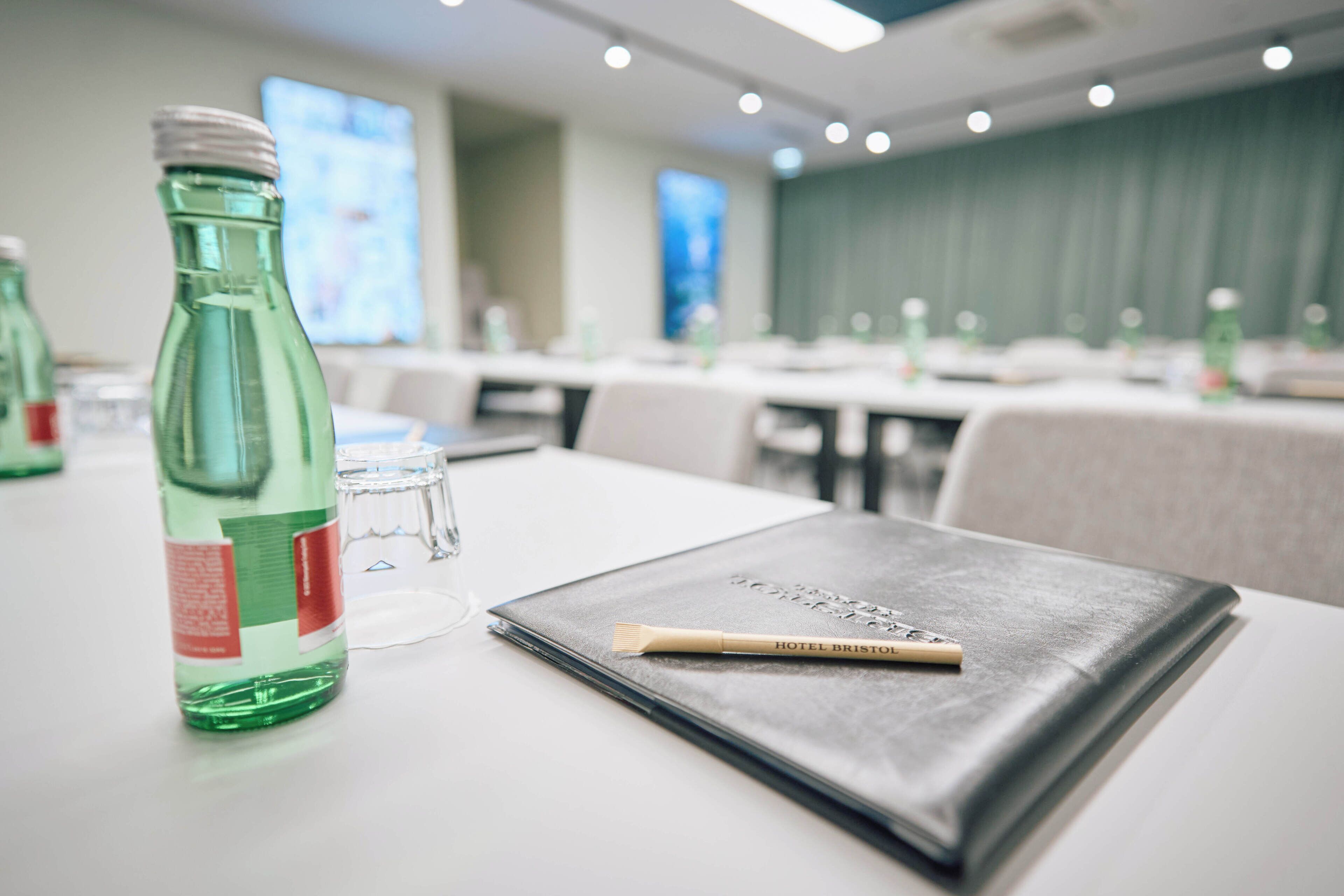 A conference room with tables set for a meeting, a green bottle, and a notebook on a table.
