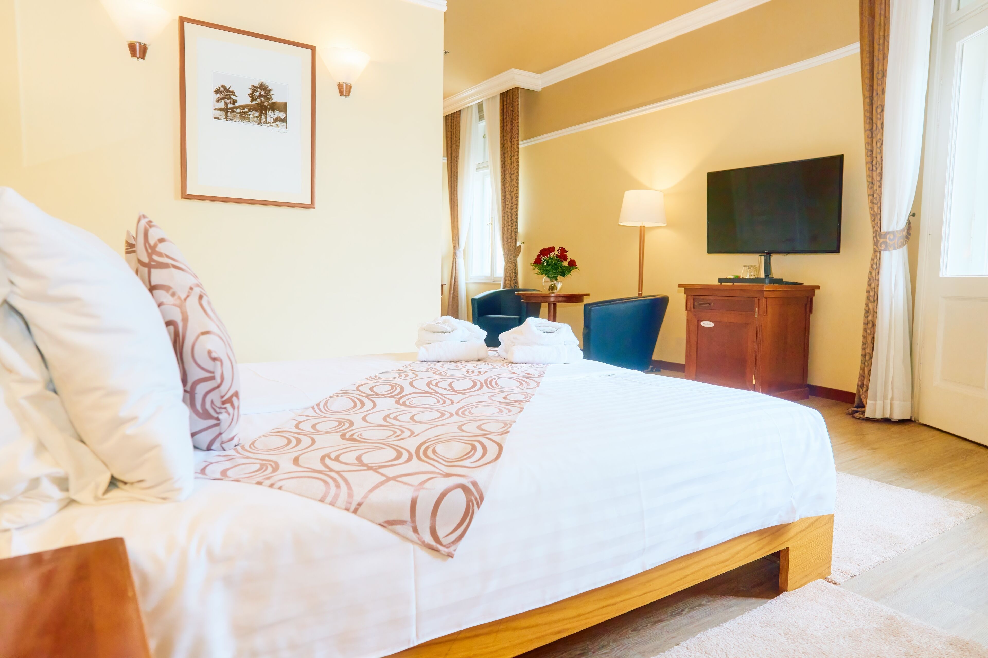 Ein Hotelzimmer mit Bett, Schreibtisch mit Stuhl, Fernseher und einem gerahmten Bild an der Wand.