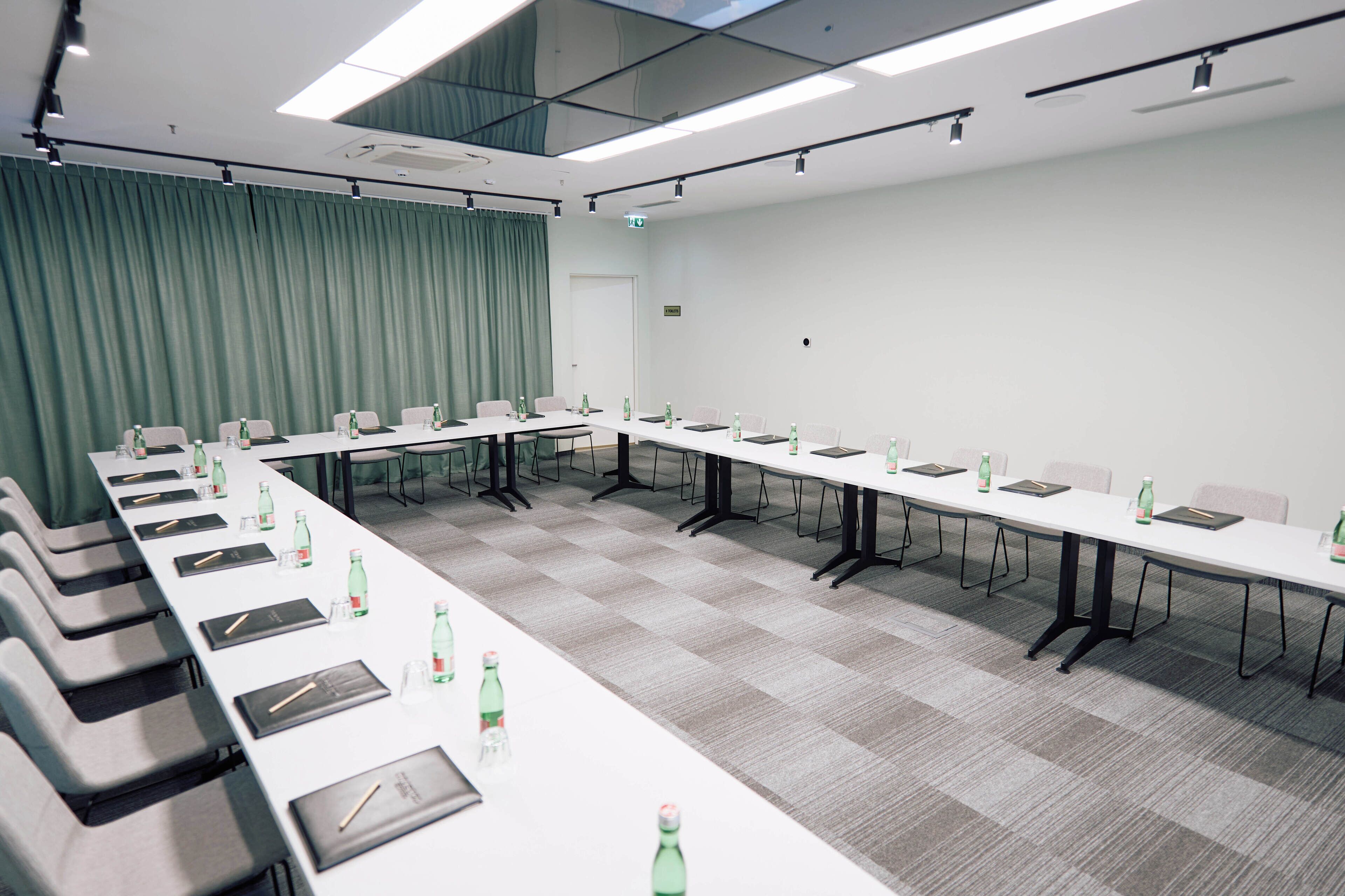 Un salón de conferencias con largas mesas, sillas y botellas de agua.