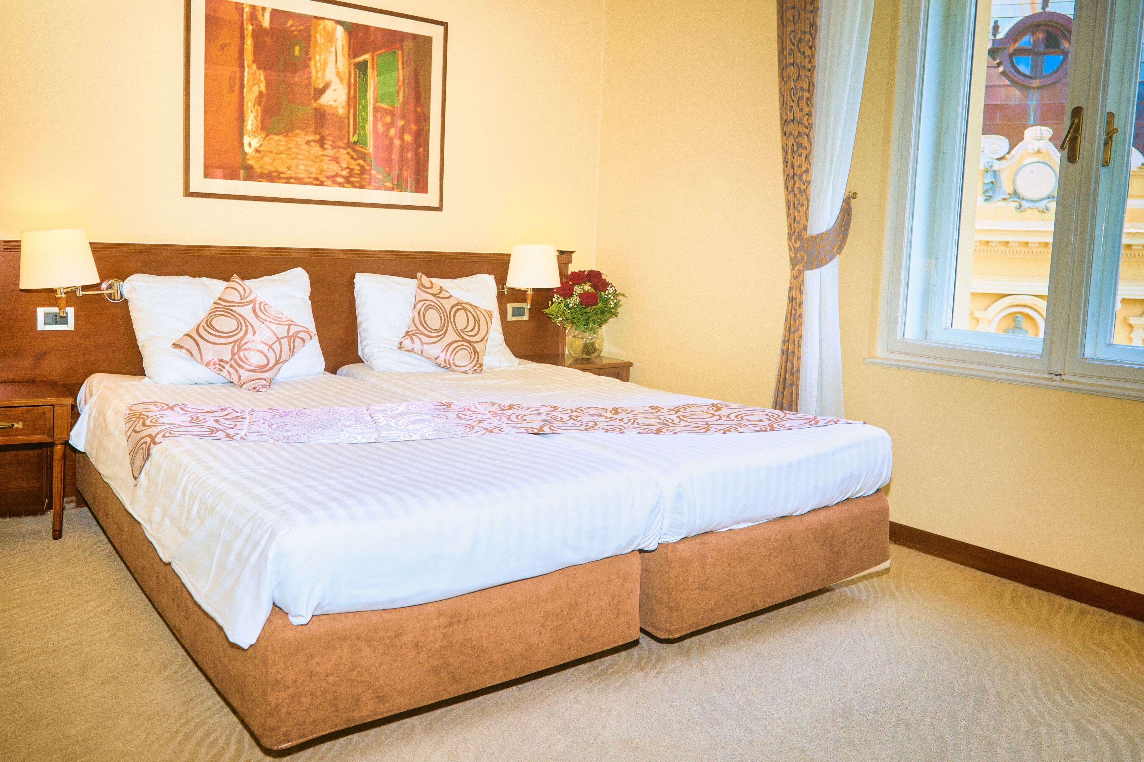 A double bed with a wooden headboard, two bedside lamps, and a nightstand with a vase of flowers.