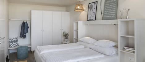 Une chambre moderne avec un grand lit, une armoire, un bureau avec un ordinateur portable et un luminaire suspendu.