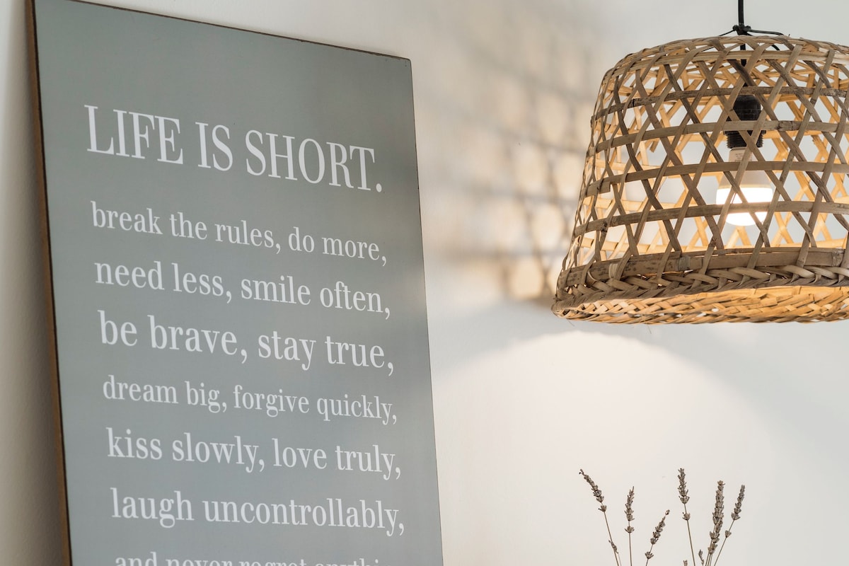 Une citation inspirante sur un mur, un luminaire suspendu en osier et deux vases ornés de fleurs séchées.