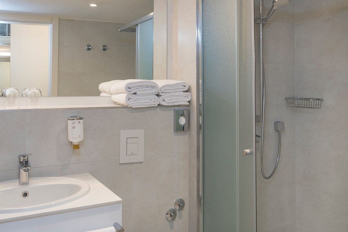 A modern bathroom with a glass-enclosed shower, a white sink, and a toilet.