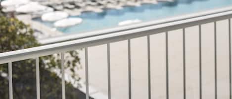 A balcony with a table and chairs, overlooking a pool area with umbrellas and lounge chairs.