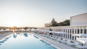 A swimming pool with lounge chairs and umbrellas, surrounded by a modern building.