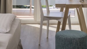 A room with a view of a lake, a wooden desk with a laptop, a white chair, and a small round ottoman.