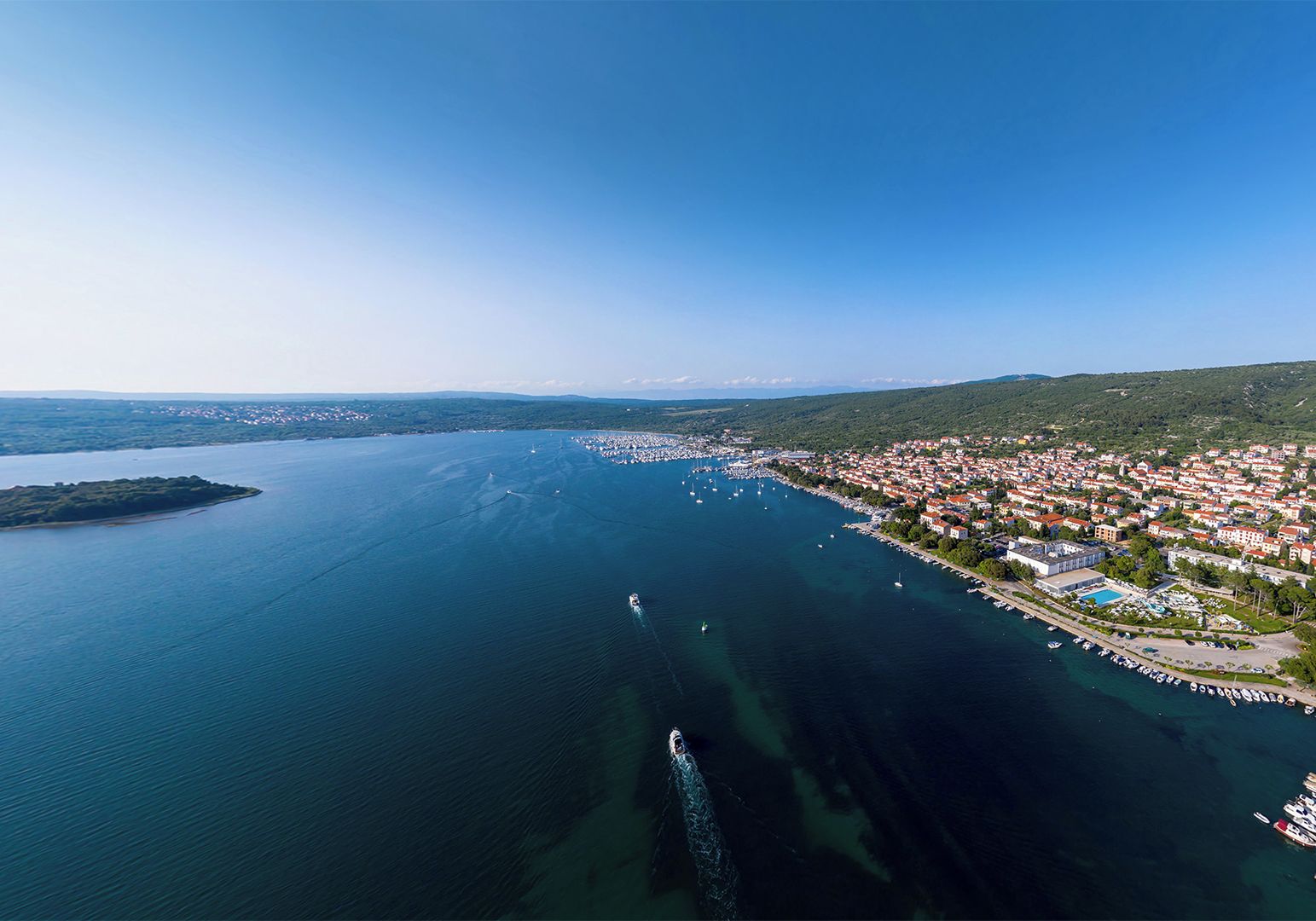An aerial view of a coastal town with a marina, houses, and a clear sky.
