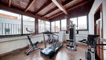 Ein Fitnessraum mit Laufbändern, einem Ergometer und Krafttrainingsgeräten, mit großen Fenstern und Holzbalken an der Decke.