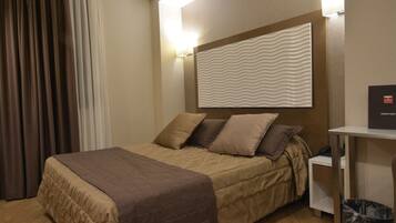 Una camera d'albergo con un letto, un comodino, un cestino e un lampadario a parete.